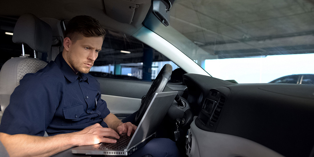 Polizist in seinem Auto. Er arbeitet am Laptop